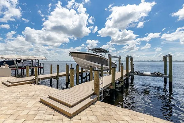 A waterfront dock featuring a boat lift holding a boat above the water, with a scenic sky in the background.