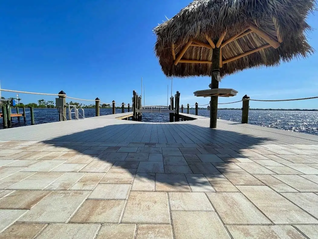 A dock with a tiki hut and paver walkway extending over the water under a bright blue sky.