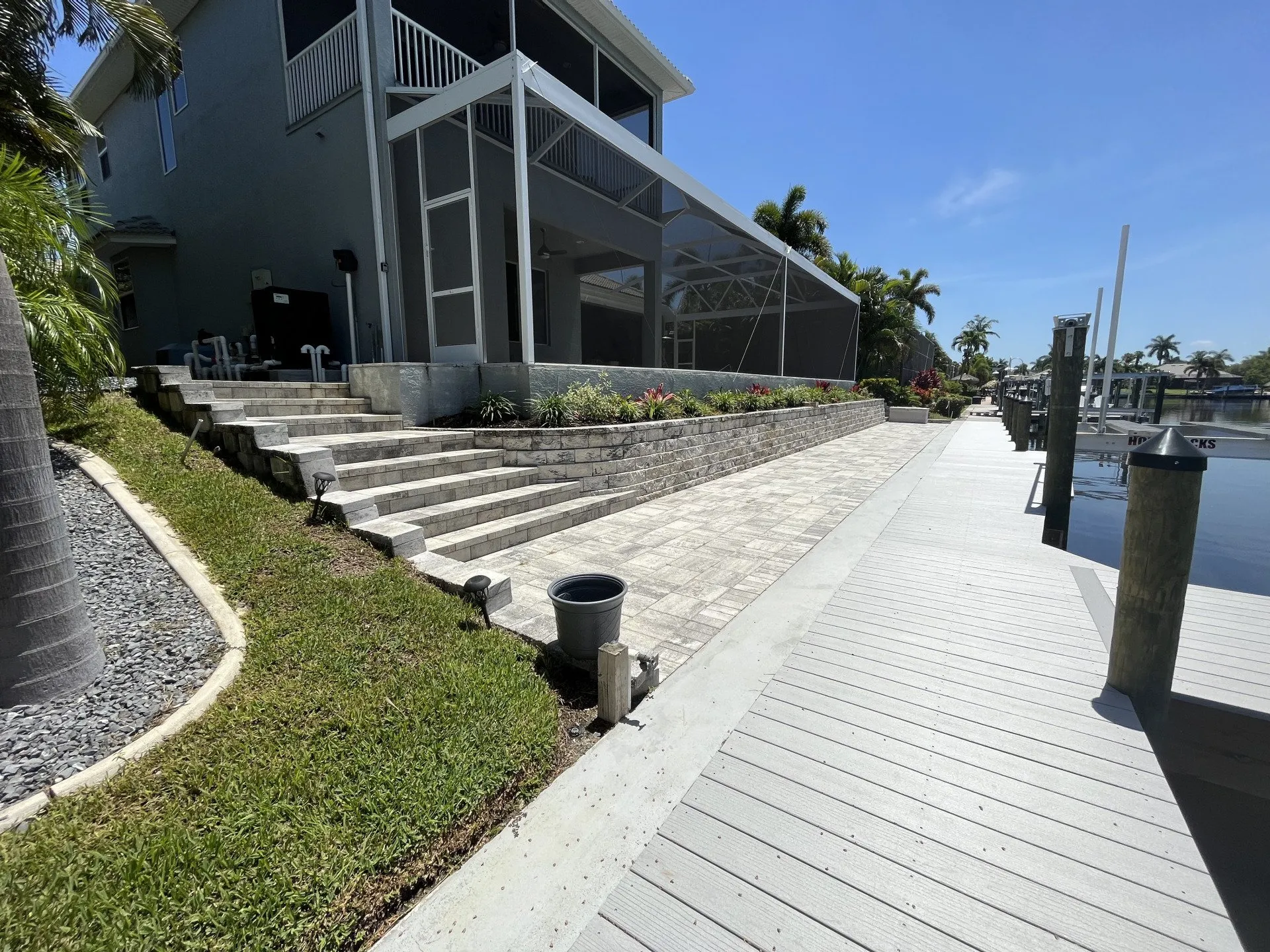 A waterfront home with a landscaped pathway, paver steps, and a dock overlooking a canal.