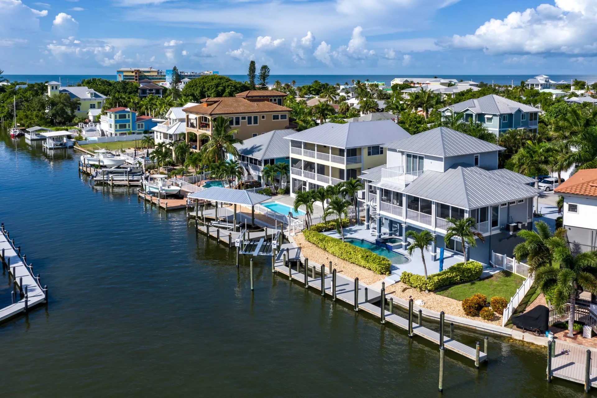 A scenic aerial view of luxury waterfront homes with private docks, lush greenery, and a clear blue sky.