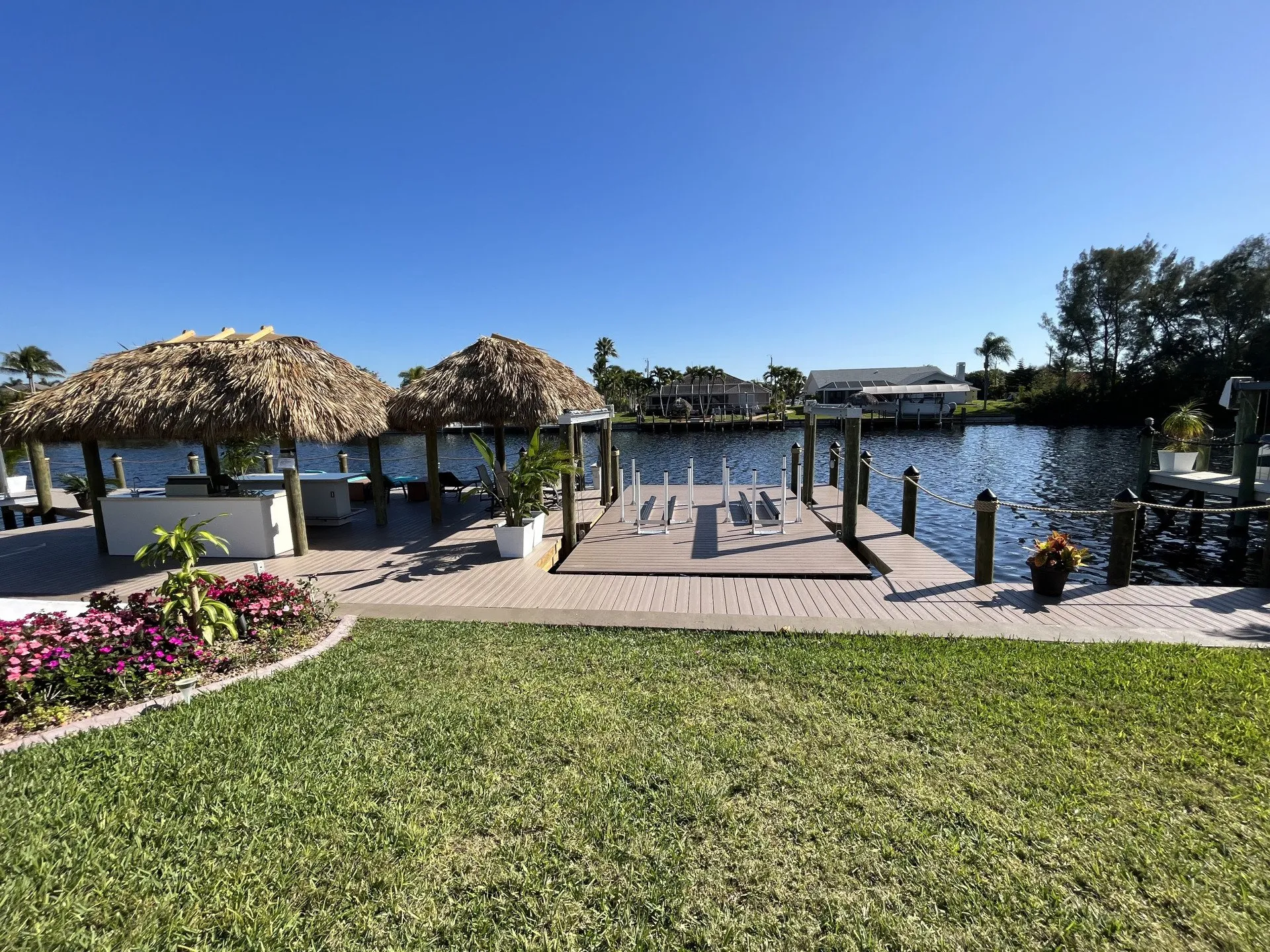 A scenic waterfront property with multiple tiki huts, a custom dock, and landscaped greenery under a clear blue sky.