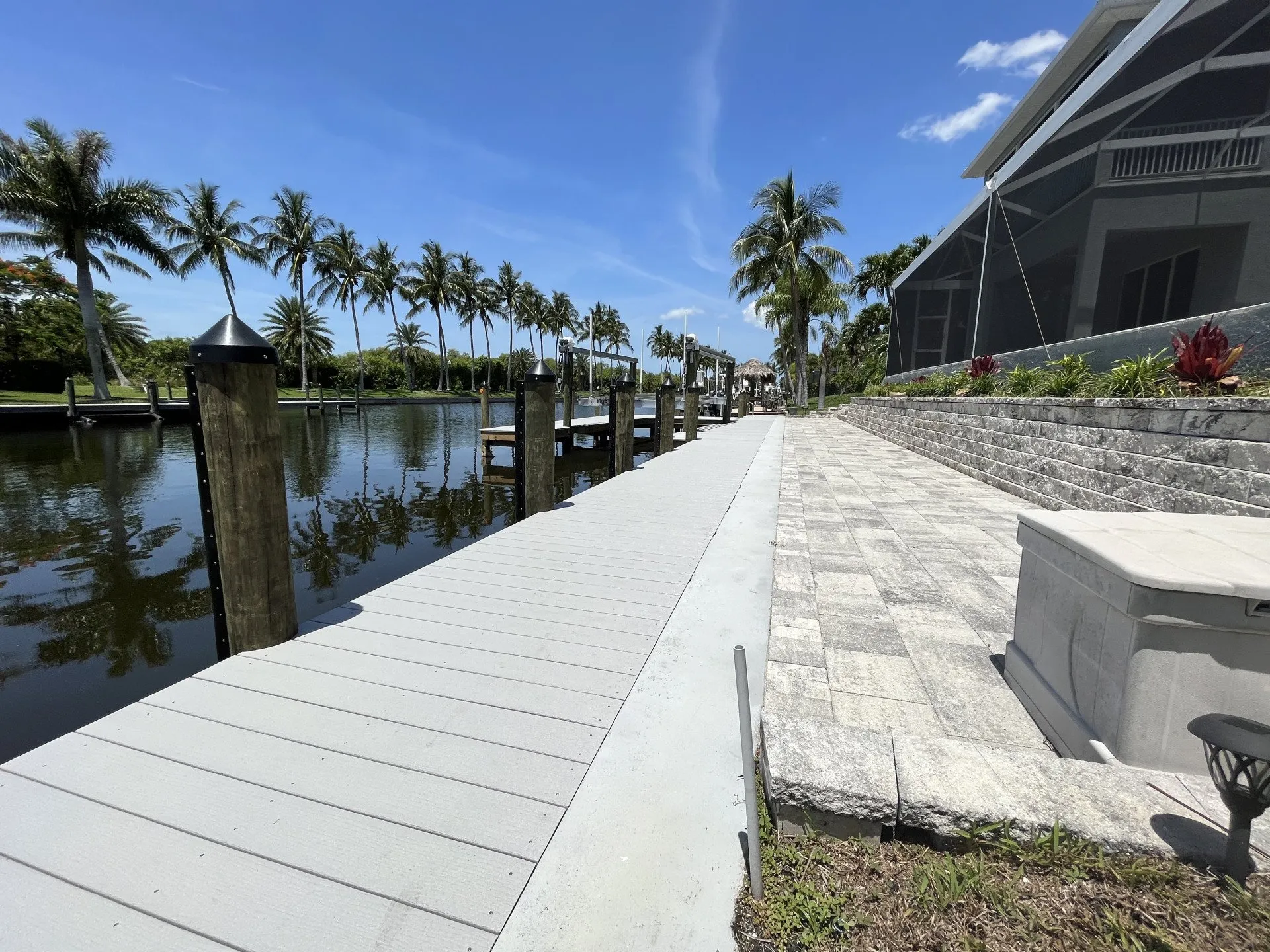 A waterfront property with a paver walkway and wooden dock along a serene canal lined with palm trees.