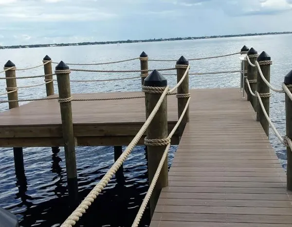 Wooden dock with rope railings and capped posts overlooking a calm waterway.