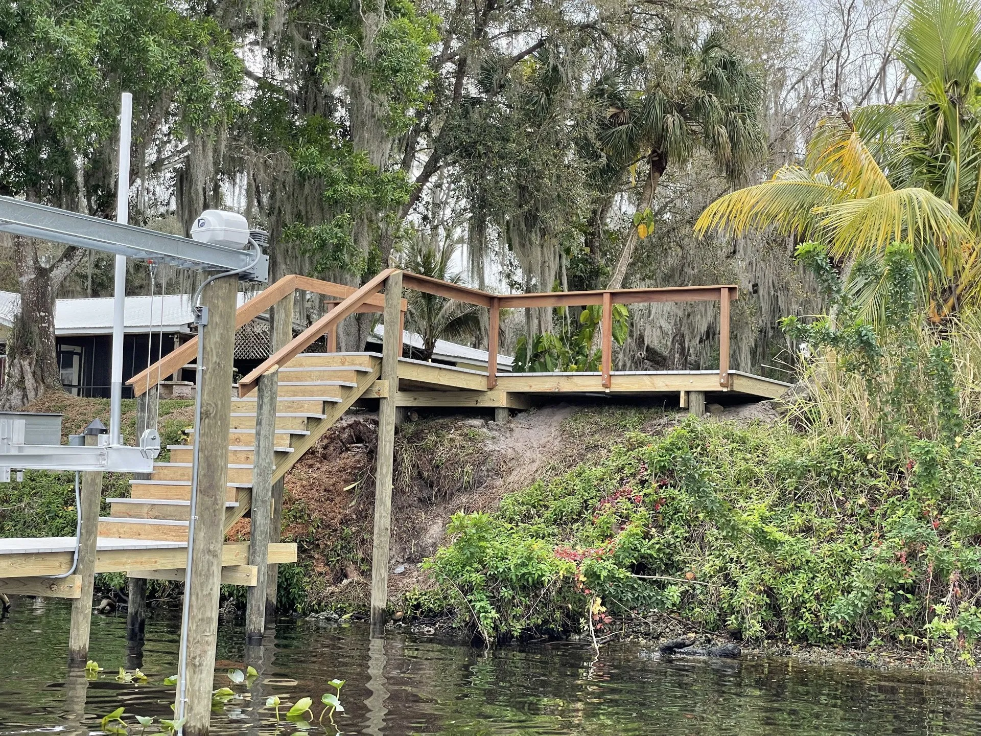 A wooden staircase and platform leading from a dock to a lush, tree-filled residential property.