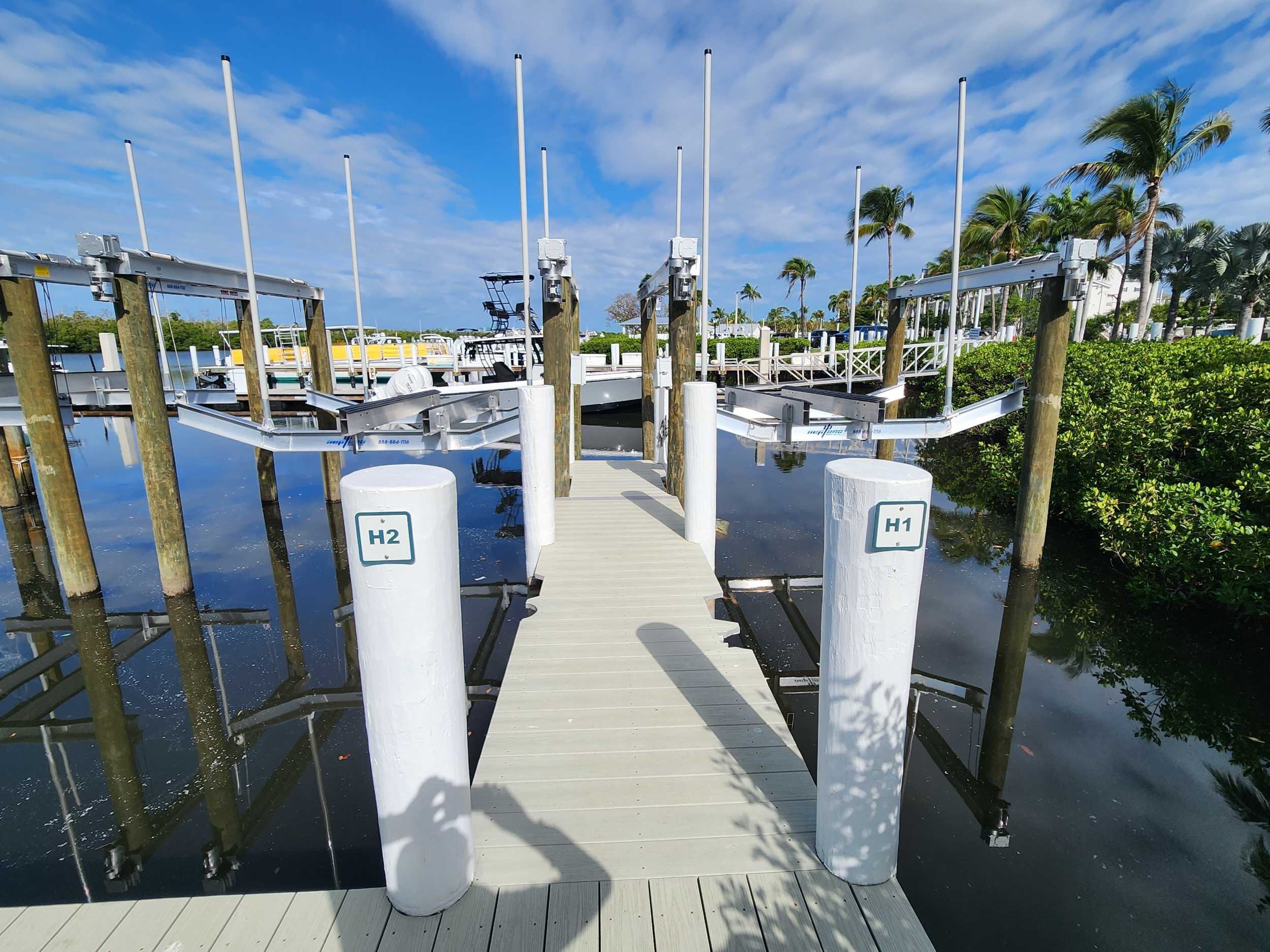 Angled cradle boat lifts at Port Sanibel Marina, positioned beside a dock slip with calm water, tropical landscaping, and marina facilities in the background.