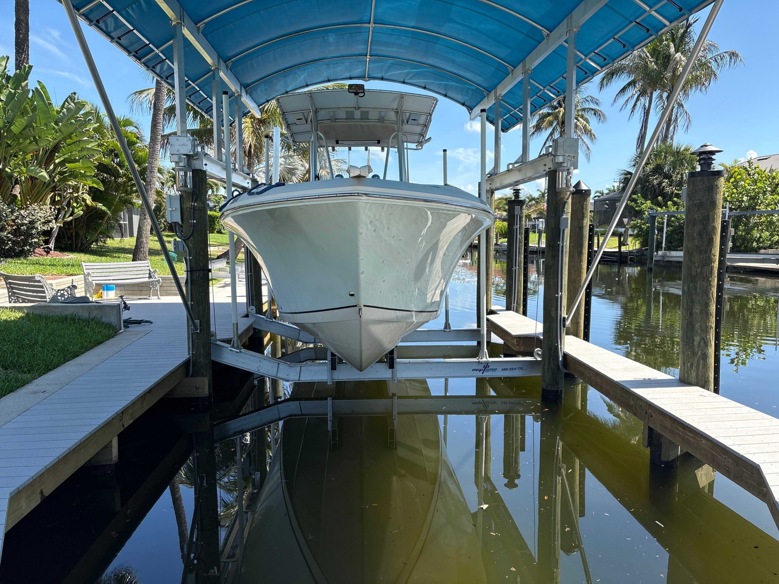 Center console boat stored on an angled aluminum boat lift beneath a blue canopy cover at a residential waterfront dock.